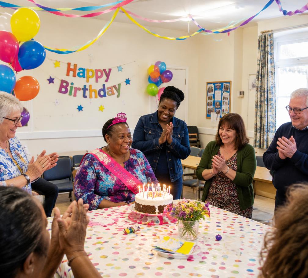 A group celebrating with balloons and a cake in a community room